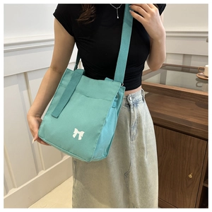 Detail view of mint green canvas crossbody bag featuring white bow print and fabric texture