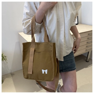 Detail view of khaki canvas tote bag with white bow print held by model in casual setting
