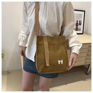 Brown canvas tote bag featuring white bow design and adjustable strap shown on shoulder