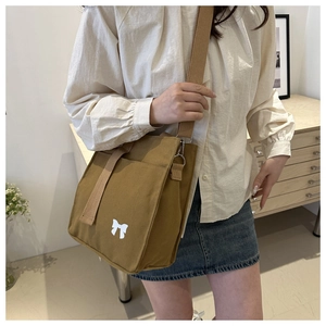 Detail view of khaki canvas tote with white bow logo and wide shoulder strap