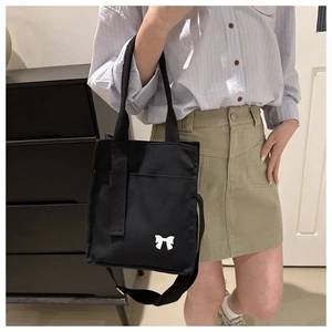 Detail of black canvas tote bag with white bow print and adjustable shoulder strap