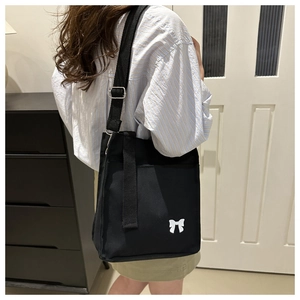 Detail of black canvas tote bag with white bow pattern and adjustable shoulder strap