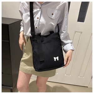 Detailed shot of a black canvas crossbody bag with a white bow print on a fashion model