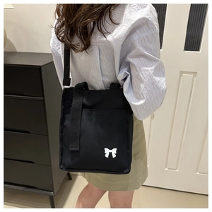 Detailed view of black canvas tote bag featuring a white bow print and woven strap
