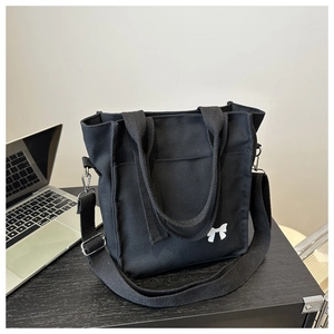 Detail of black canvas tote bag featuring white bow embroidery and adjustable shoulder strap