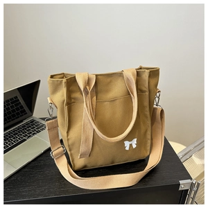 Detail of khaki canvas tote bag with white bow accent and adjustable shoulder strap