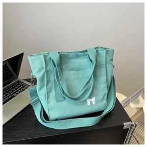 Mint green canvas tote bag with white bow print on a black wooden desk next to a laptop