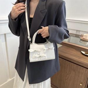 White minimalist mini handbag with decorative bows and metal dots, styled with grey suit