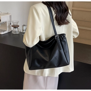 Detail view of large black leather tote bag with adjustable silver buckle on a shoulder strap