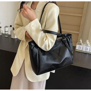 Detail of black matte leather tote bag with side pleats and metal buckle on strap