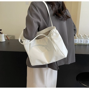 Detail view of large white tote bag with matte leather texture on a grey blazer model