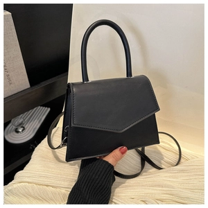 Detail of a black faux leather trapezoid handbag with top handle on white fabric