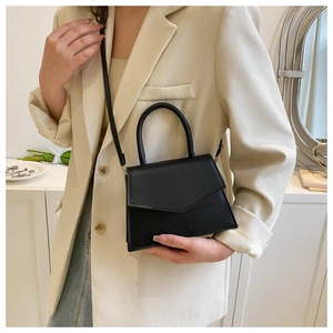 Close-up of minimalist black trapezoid handbag styled with a modern cream blazer and jeans