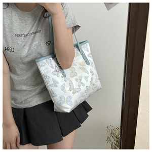 Detailed view of the butterfly embroidery and light blue leather handles on a tote bag