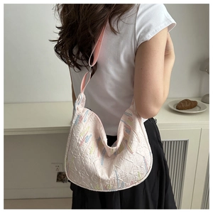 Detail of pink embroidered dumpling bag with textured patterns and textile shoulder strap