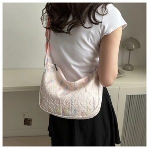 Detail of light pink embroidered tote bag with monogram pattern shown on a model