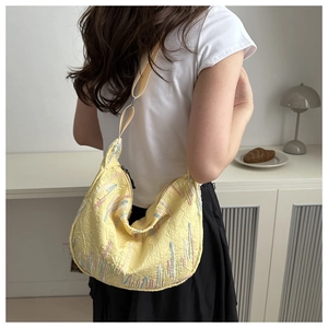 Detail of light yellow crescent bag with textured fabric and colorful embroidery accents