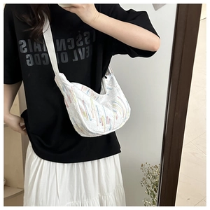 Detail of white half-moon bag featuring colorful embroidery and wide shoulder strap