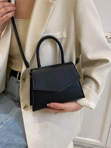 Minimalist black trapezoid handbag with envelope flap shown on a model in beige blazer