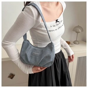 Detail of grey-blue pleated shoulder bag with oval brand tag in a minimalist interior