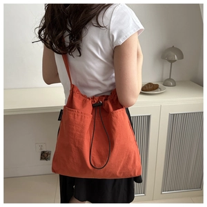 Detail of orange nylon bucket bag showing drawstring closure and front double pockets