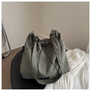 Detail of moss green drawstring bucket bag showing crinkled nylon fabric and side logo