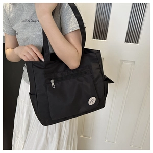 Detail of black nylon tote bag with functional side pockets and circular luck patch