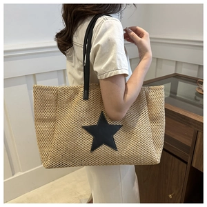 Close-up of woven straw tote bag featuring a black star patch and slender leather straps