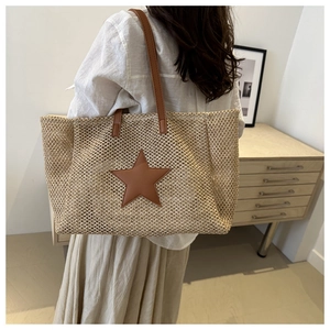 Rear view of a woven straw tote bag with a brown leather star patch on a model back