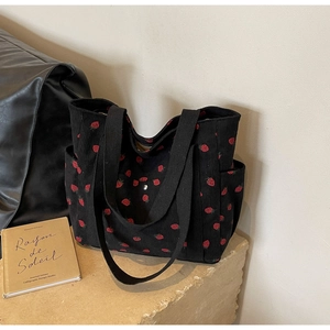 Gros plan du sac cabas en velours côtelé noir avec motifs de fraises rouges et poignées