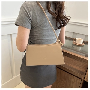 Detail of a beige baguette shoulder bag with embossed fashion text and knot strap detail