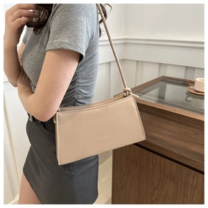 Detail of minimalist beige baguette bag with gold FASHION text and slender shoulder strap