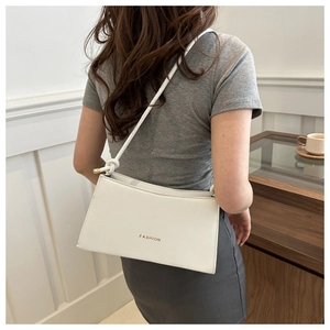 Detail of white leather shoulder bag featuring gold metal knots and Fashion lettering