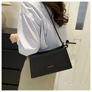 Detail of minimalist black underarm bag featuring gold FASHION text and matte finish