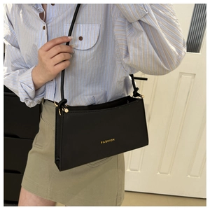 Detail of minimalist black faux leather bag with golden Fashion text on the front