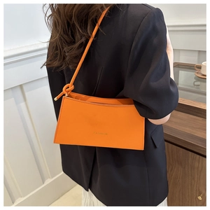 Detail of orange faux leather shoulder bag with gold 'FASHION' lettering and knotted strap