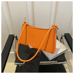 Detail of vibrant orange baguette bag with gold Fashion text and knotted strap detail