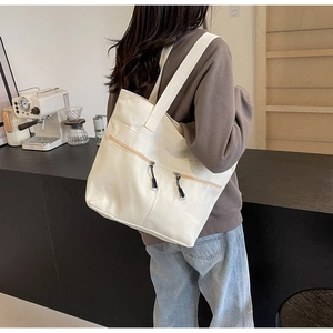Detail of off-white canvas tote bag featuring double front zipper pockets in a cafe setting