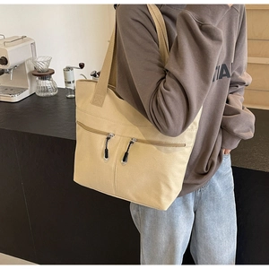Detail of beige canvas tote bag featuring double front zipper pockets and woven straps