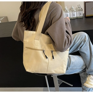 Detail of beige canvas tote bag with front zipper pocket and reinforced strap on shoulder