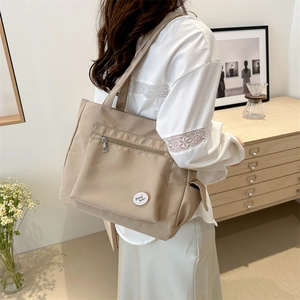 Minimalist beige nylon tote bag with large zipper pocket shown in a lifestyle setting