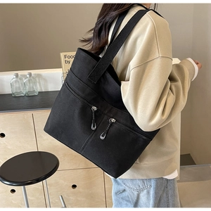 Detailed side view of a large black canvas tote bag with front zipper pockets