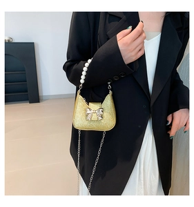 Detail of mini gold glitter evening bag with pearl handle and metal bow decoration