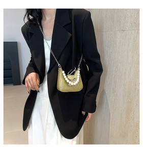 Detail of sequin saddle bag with pearl handle and silver bow charm on black dress