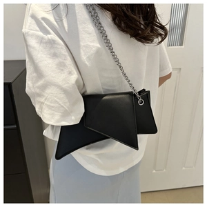 Detail of a black geometric crossbody bag with a silver chain strap worn by a model