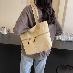 Minimalist beige canvas tote bag with dual front zipper pockets shown on a shoulder