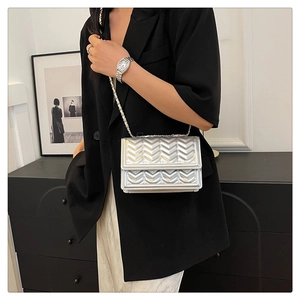 Detailed view of silver quilted crossbody bag with luxury metal chain strap on model