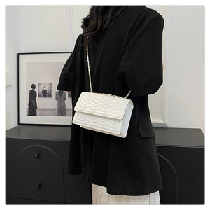 Detail of white quilted crossbody bag with V-shaped stitching and golden metal chain