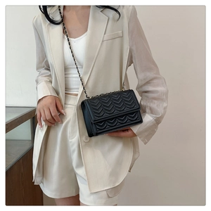 Close-up of black wave-quilted chain bag worn over a stylish beige blazer