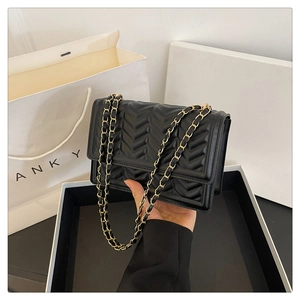 Close-up of black quilted shoulder bag featuring V-shaped texture and gold chain strap
